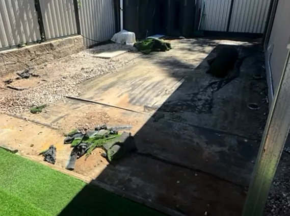 Backyard before, with broken concrete, loose rubble and uneven ground