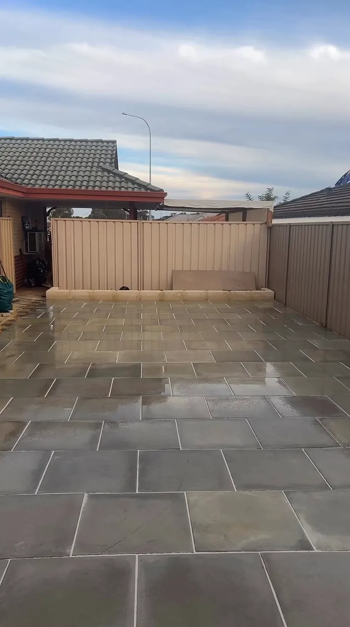Same backyard paved edge to edge in large grey slabs, freshly washed