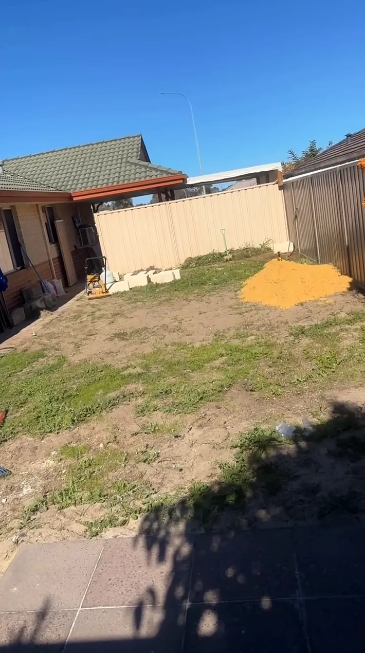 Backyard before, with patchy grass, bare dirt and a pile of sand