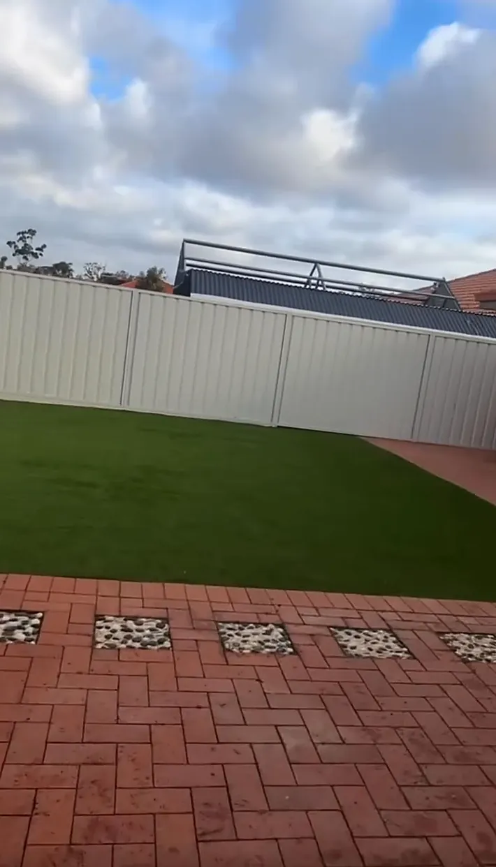 Fresh lawn meeting red brick paving with decorative pebble squares