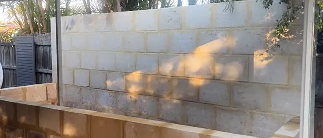 Same backyard after, with a tall limestone block retaining wall and a raised limestone garden bed in front