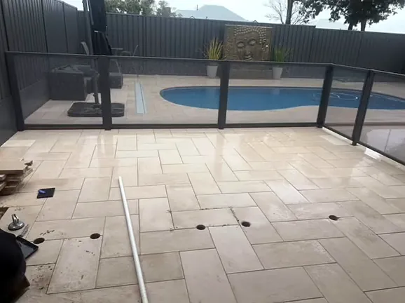 Pale pool surround paving, freshly washed, behind a glass pool fence