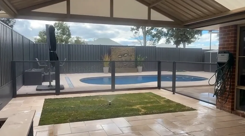 Covered alfresco opening onto new pale paving around a pool, with a rectangle of lawn set into the paving