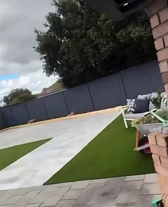 Synthetic lawn divided by a pale paved path in a backyard